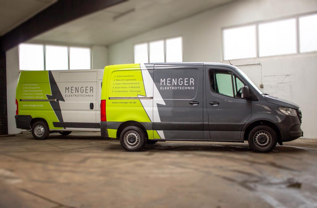 Zwei Lieferwagen der Firma MENGER Elektrotechnik mit modernem Design parken nebeneinander in einer hellen Lagerhalle.