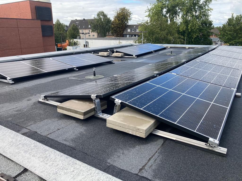 Photovoltaikanlage mit geneigten Solarmodulen auf Flachdach, montiert mit Betongewichten zur Stabilisierung der Unterkonstruktion.